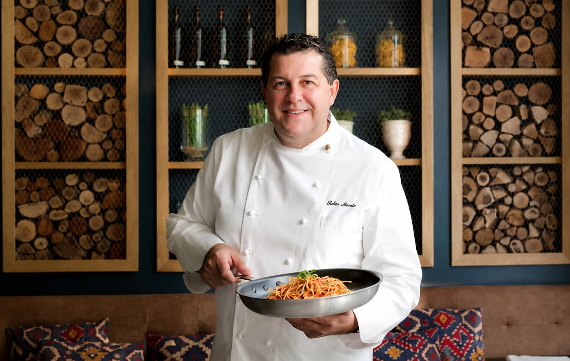 El chef Fabio Morisi sosteniendo una sartén de spaghetti con tomate y albahaca en ÔVEN
